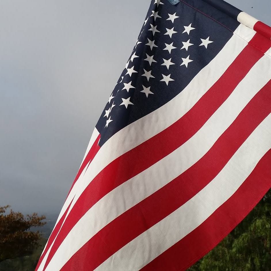 American flag waving against a gray, overcast sky.